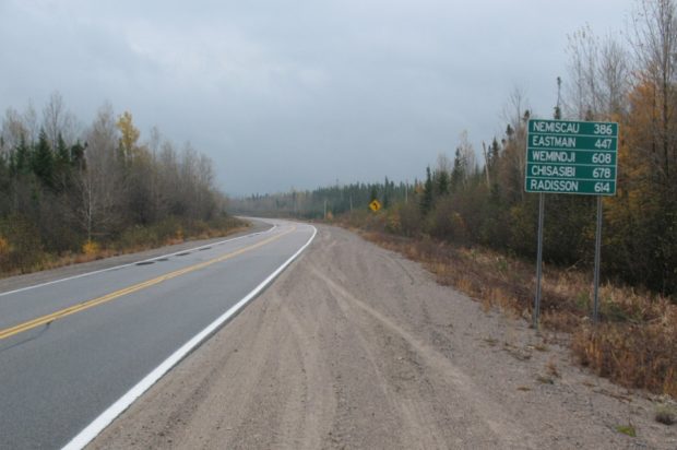 Highway through the forest and road sign showing distance to Cree towns.