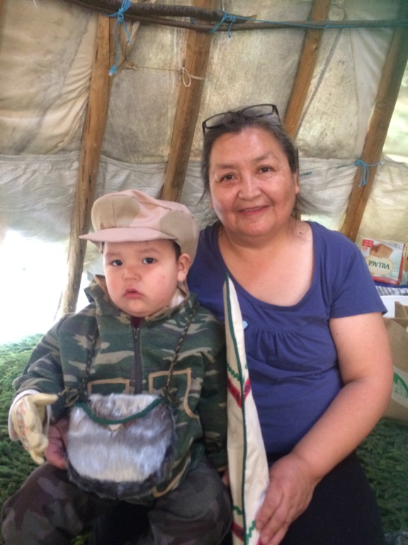 A little boy in a hat sitting with his grandmother sitting in a traditional teepee