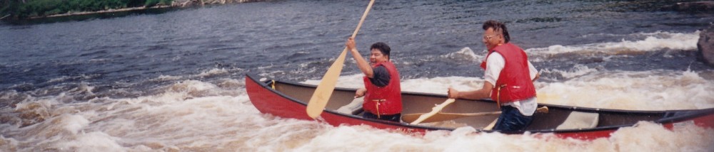 Smiling men wearing red life jackets in a canoe