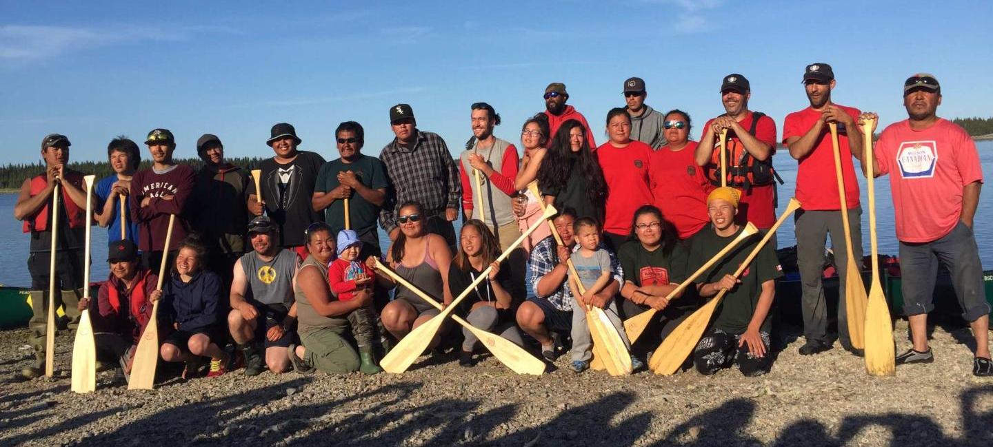 Group of smiling men and women holding canoe paddles.