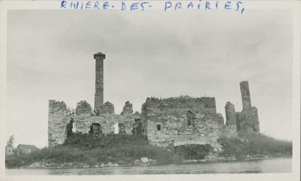 Vintage black and white photograph of stone ruins on the shores of a river. This is a former mill that was destroyed. On the top of the white border are the handwritten words “Rivière-des-Prairies.”