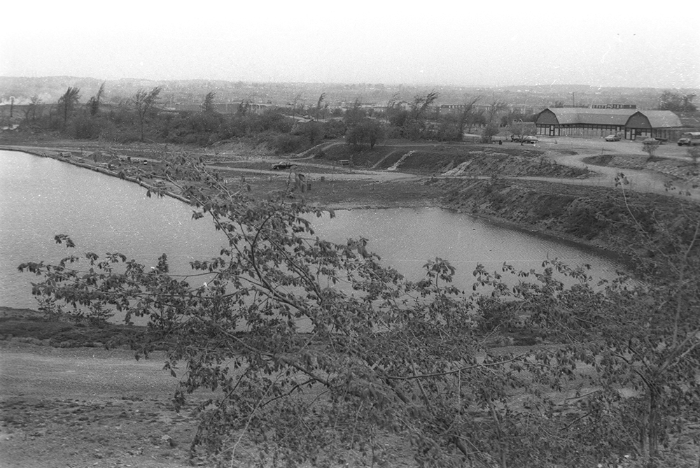 Photographie en noir et blanc d’une ancienne carrière en processus de réhabilitation. On y voit un lac et une serre au loin. Il s’agit aujourd’hui du Centre de la nature de Laval. 