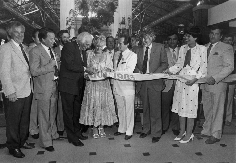 Black and white photograph of formally dressed women and men assembled to cut the ribbon for the official opening of the Laval public market.