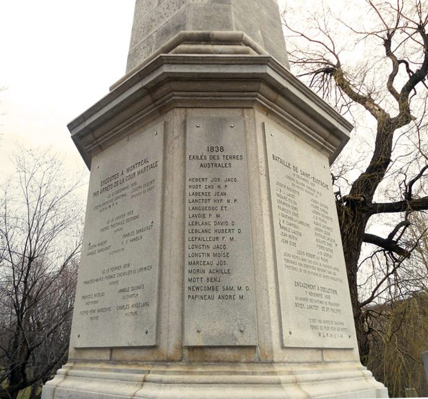 Picture of a stone monument dedicated to the patriots. It is surrounded by leafless trees.