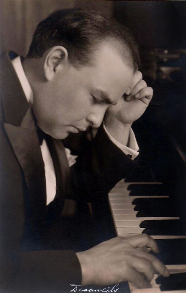 Black and white picture of Auguste Descarries at the piano; he looks thoughtfully at the keyboard with one hand on his forehead and the other on the keyboard.