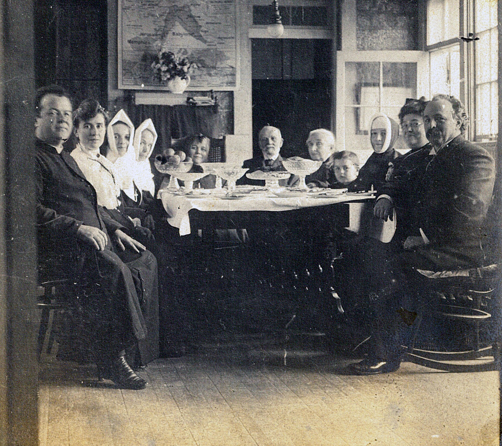 Black and white picture. These are 11 members of the LePailleur family sitting at the table. We can see Georges-Marie, Sister Agnès, Alfred-Narcisse, Philomène, Célina-Elmire and Joseph-Adélard.