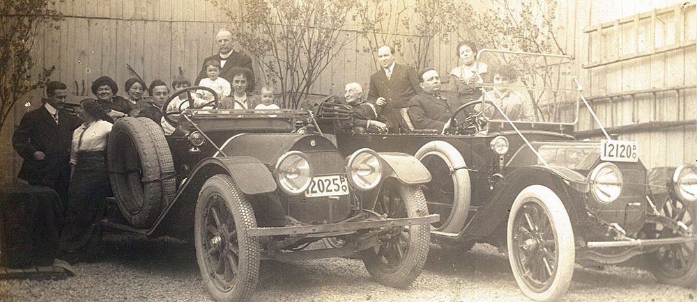 Black and white picture of a group of people sitting in two cars from the 1920s. In the group are Théophile and Célina-Elmire LePailleur, Joseph-Adélard Descarries and Philomène Dalton. Five people are standing on the ground or on the cars steps.