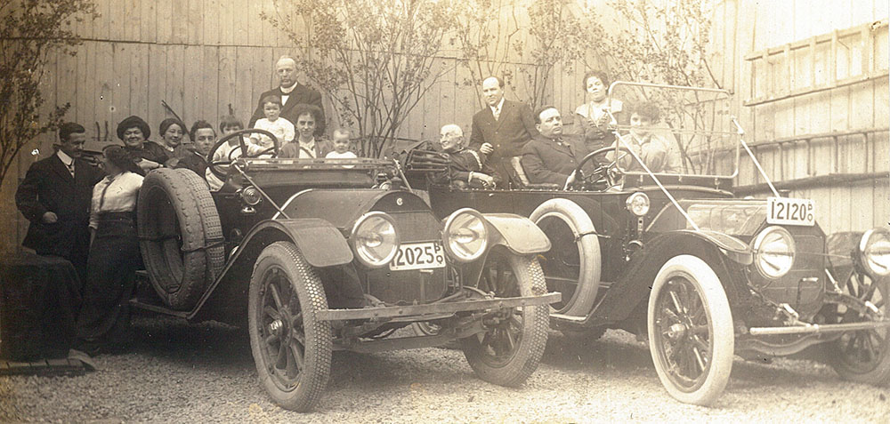 Black and white picture of a group of people sitting in two cars from the 1920s. In the group are Théophile and Célina-Elmire LePailleur, Joseph-Adélard Descarries and Philomène Dalton. Five people are standing on the ground or on the cars steps.