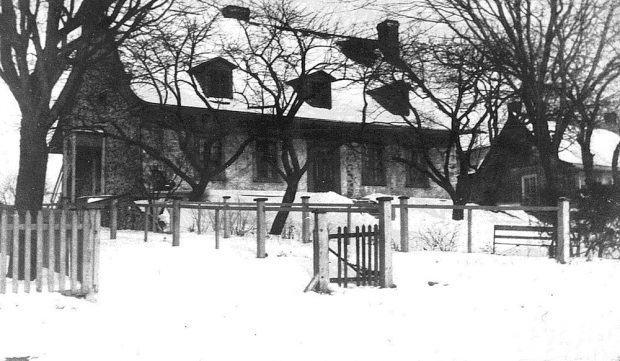 Black and white picture of the Maison LePailleur in winter, a traditional Quebec house built of stone with a pitched roof and three dormers.