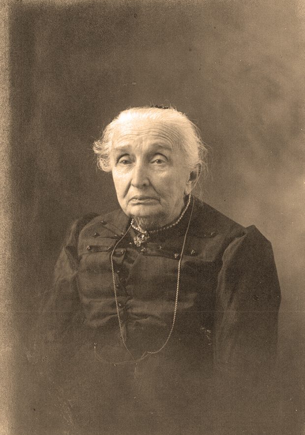 Sepia portrait of Philomène Dalton at an advanced age. She is wearing a black dress, a pearl necklace and a cross.
