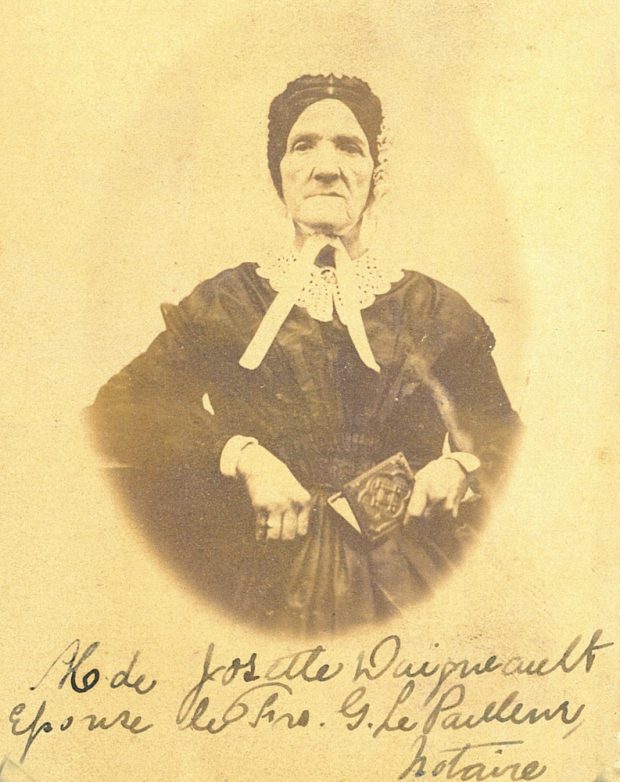 Black and white picture of widow Josephte Daigneault (wife of notary F-G LePailleur) in a black dress and white cap. She holds a small album in her left hand.