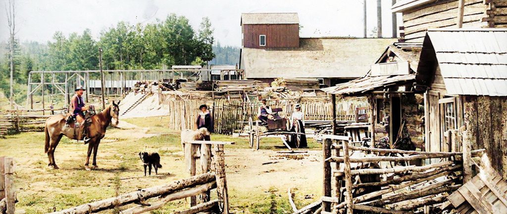 Man on horseback, dog and buggy in front of wooden buildings and fences