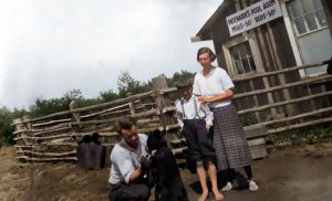 Family of 3 with bear cub in front of wooden building and fence