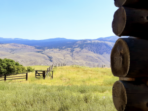 Profile of log building before fenced field and mountains