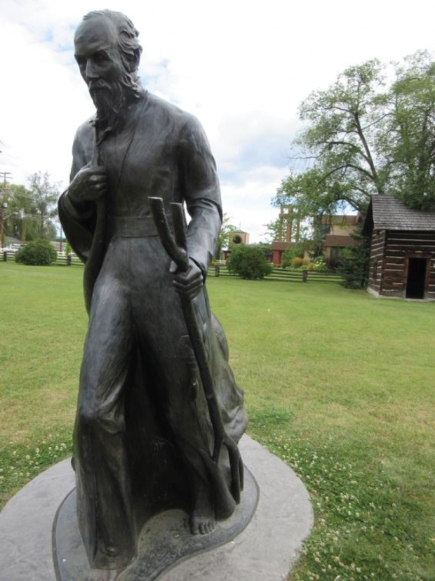 Statue of priest in front of log cabin