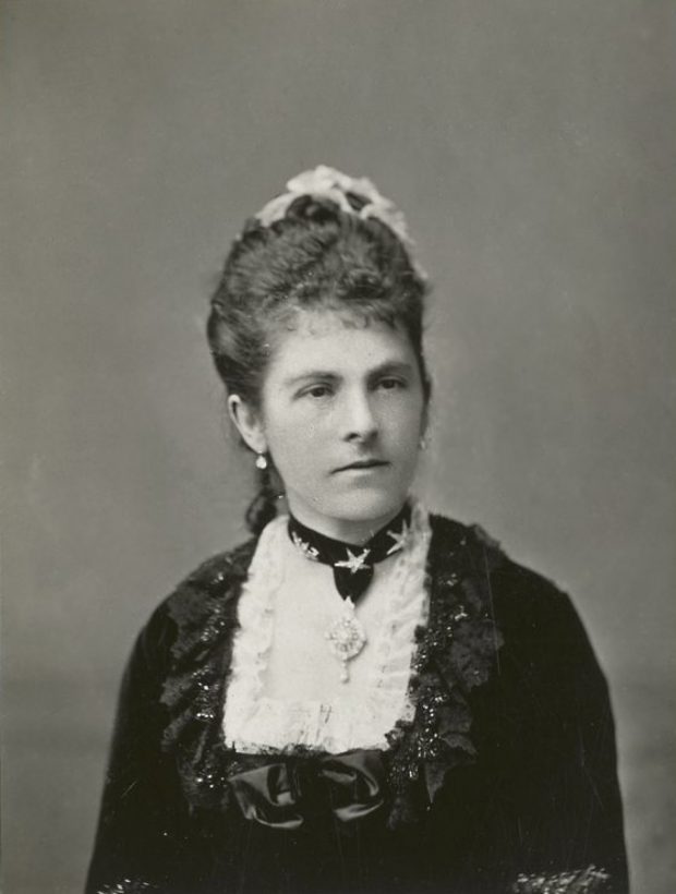 Black and white photograph of the head and shoulders of Lady Dufferin, with her hair swept up, and a formal dress with a lacy squared bodice and jewelled necklace.