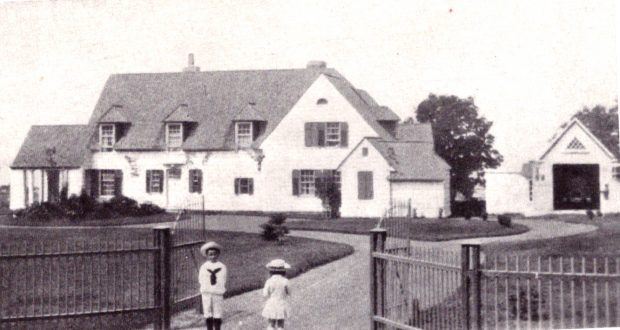 Sepia-toned photograph of an expansive house (Kenneth Molson's estate) surrounded by an iron fence with gate, and two small children in sailor suits in the foreground.