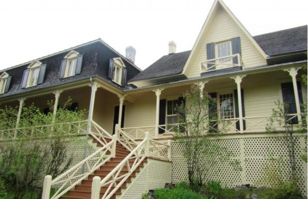 View of Villa Les Rochers, a large house and verandah, plus steps leading up to it, taken from the lawn. The sky is colorless.