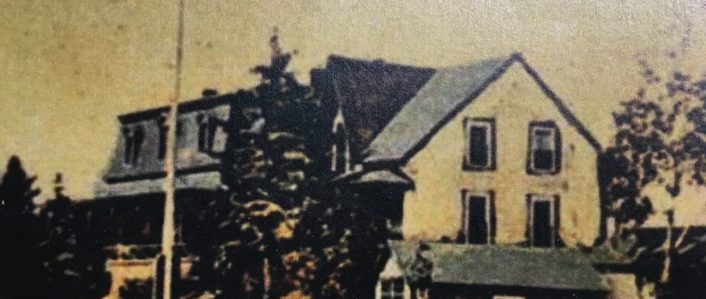 Hand-coloured (originally black and white) photograph of a large house (Villa Les Rochers) with a flagpole in front of it, and a shed attached to the side of it.