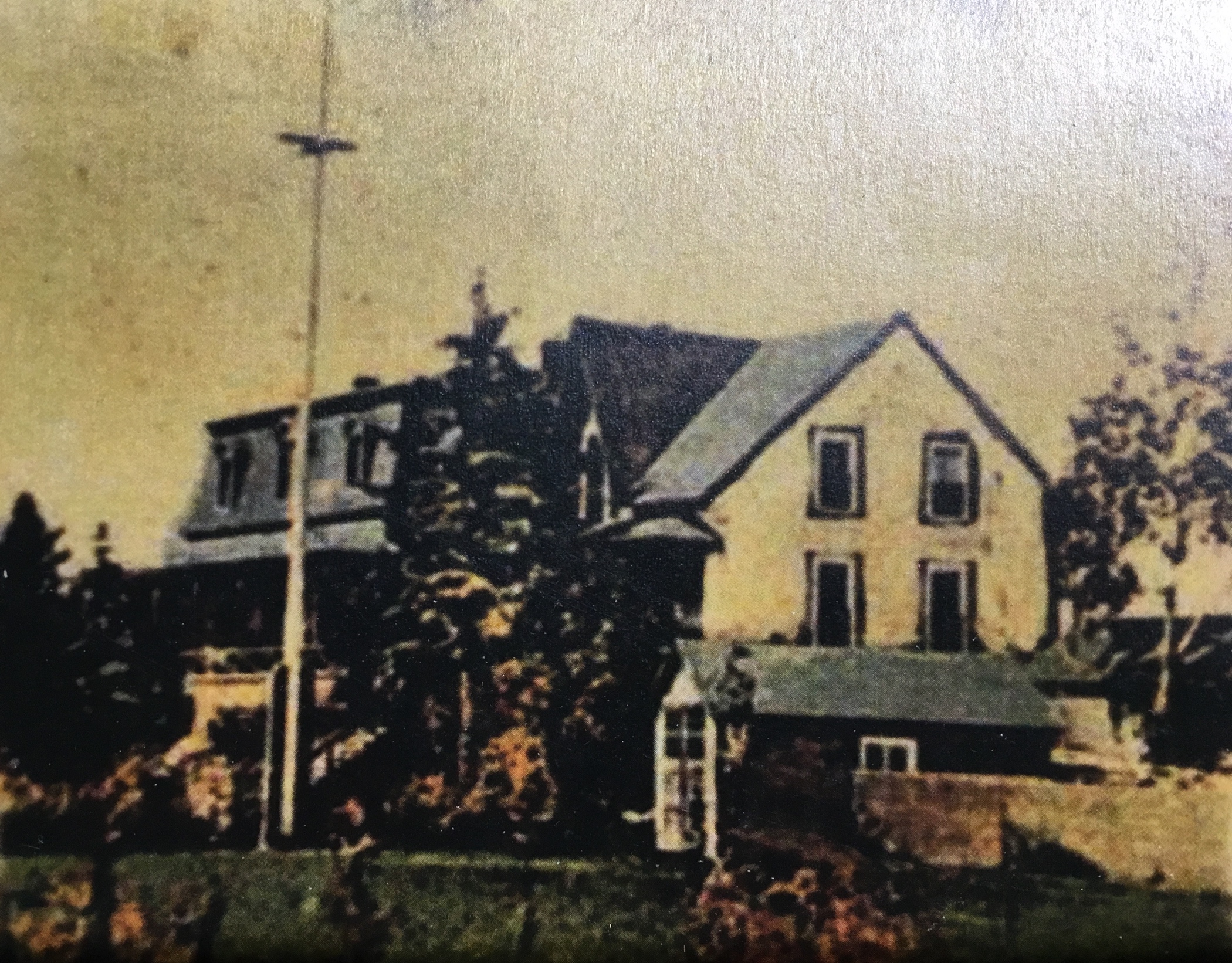 Hand-coloured (originally black and white) photograph of a large house (Villa Les Rochers) with a flagpole in front of it, and a shed attached to the side of it.