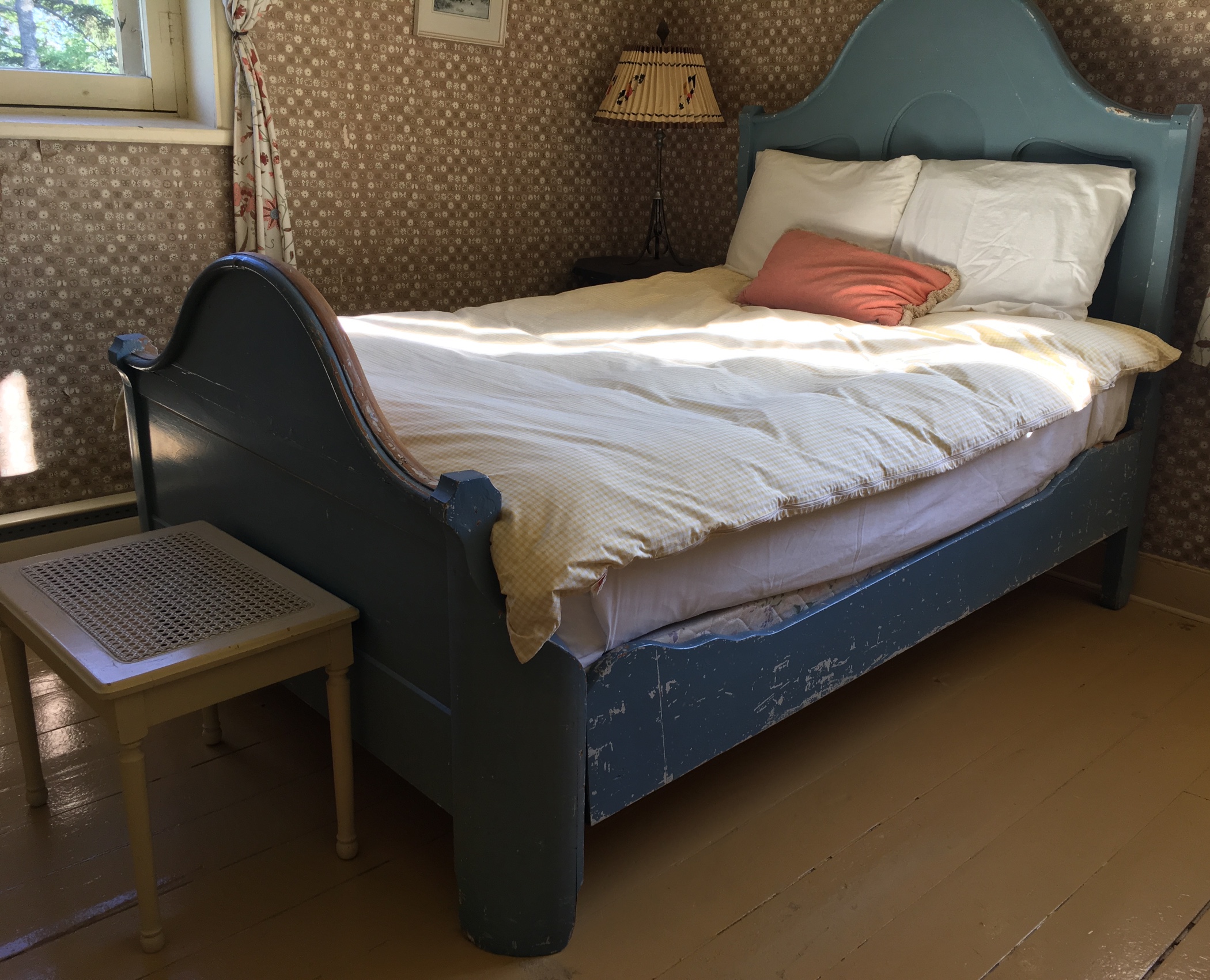 A colour photograph of Sir John A. Macdonald's bed, a wooden three-quarter size bed, featuring a tall headboard and smaller footboard, with scuffed blue paint especially along the sideboards.