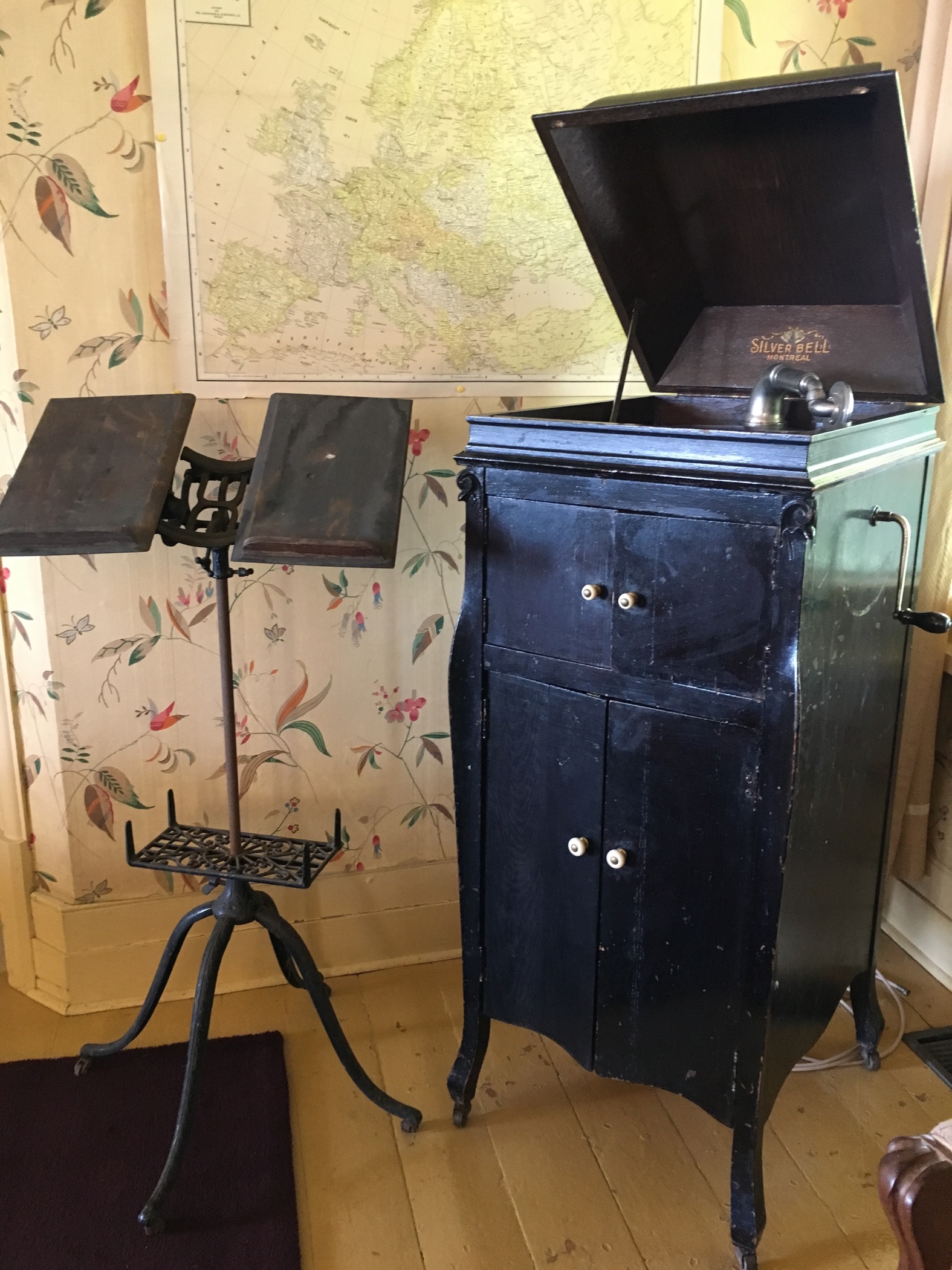 A colour photo of an old wooden victrola, its lid propped open, and next to the victrola is a cast-iron music stand.