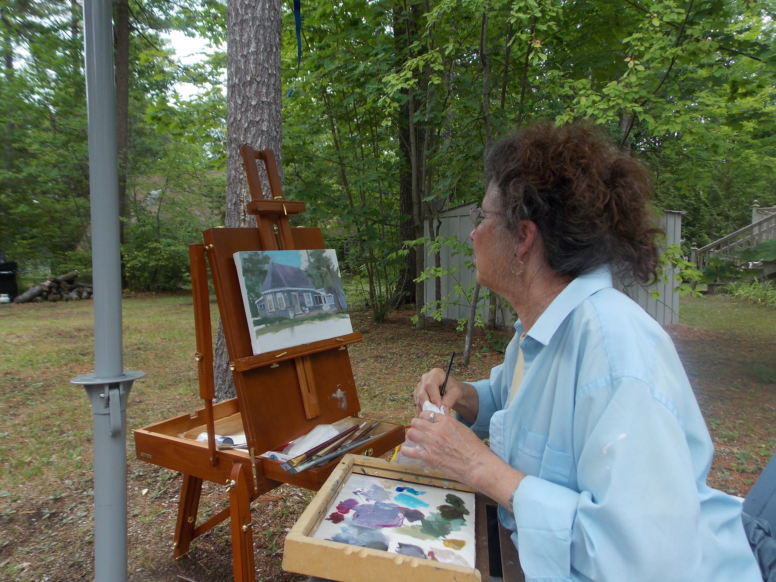 Image of someone seated outside at an easel painting a cottage.