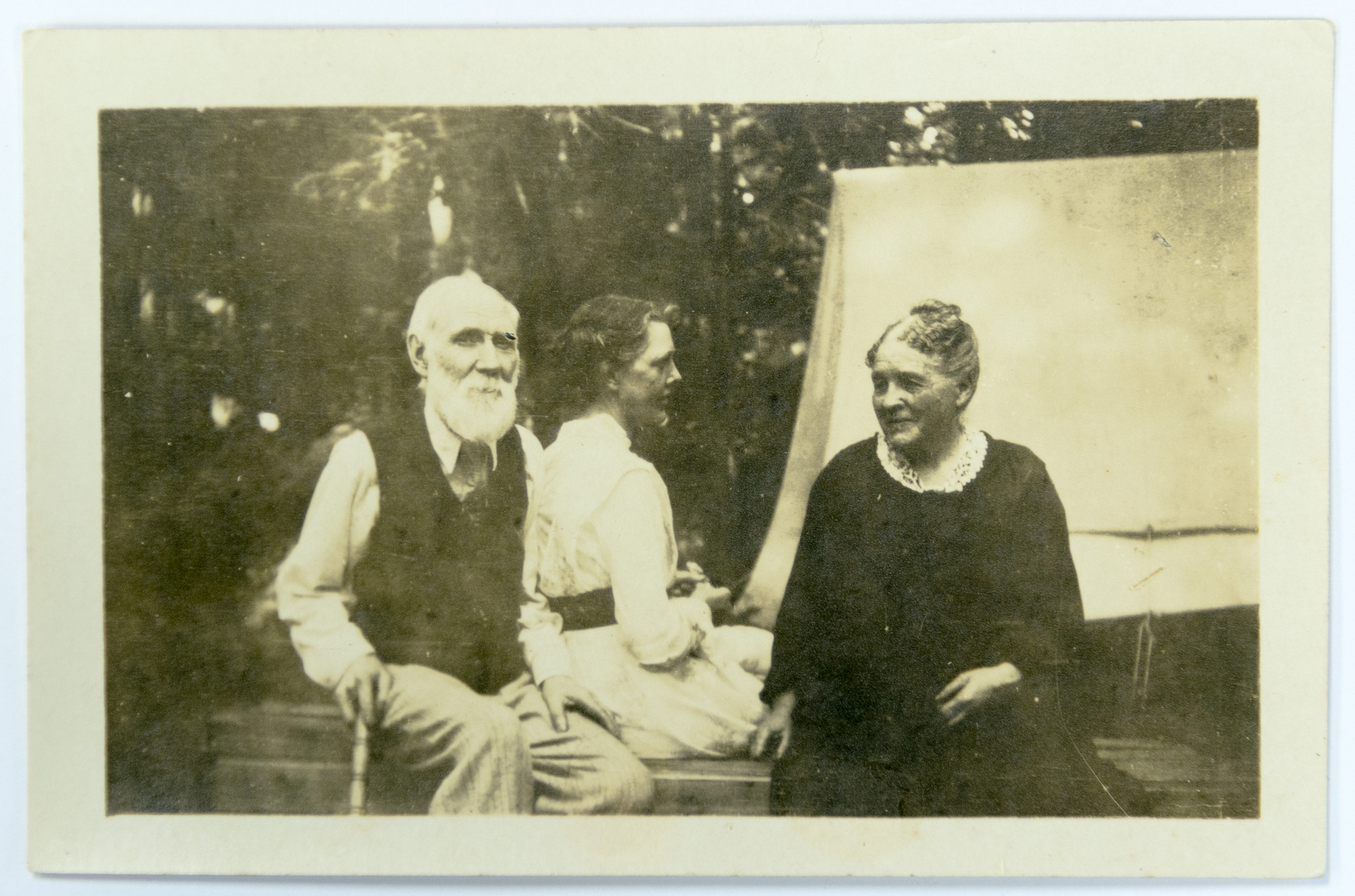 One man with beard and two women seated outside in informal attire.
