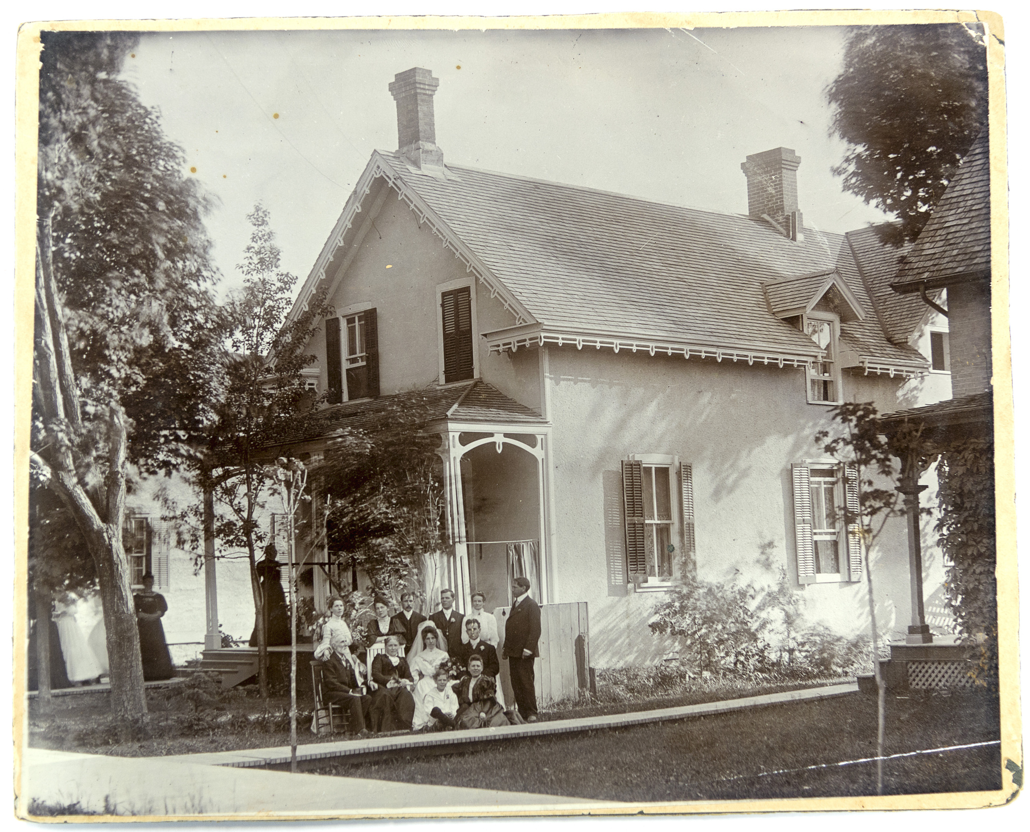 Black-and-white image of a wedding party gathered beside a house.