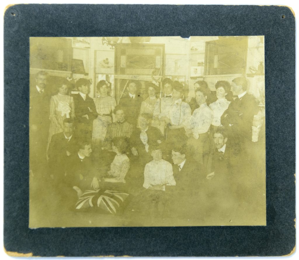 Image of a large group of people in formal attire gathered inside of a room with pictures mounted on the walls.