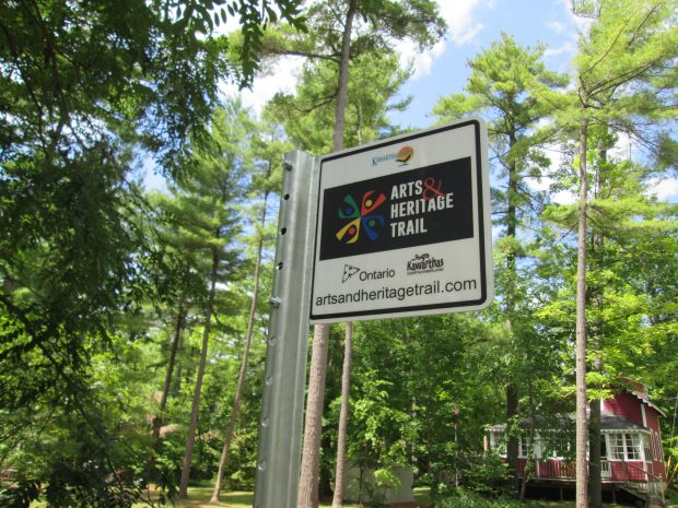 Metal sign surrounded by trees with building in lower right