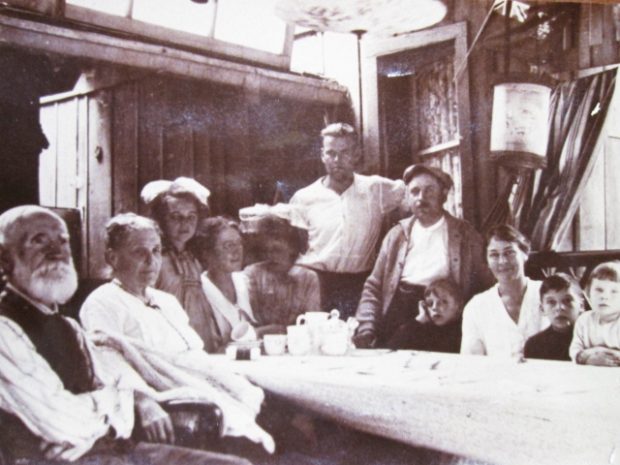Image of black-and-white photograph showing eleven people seated around table on porch
