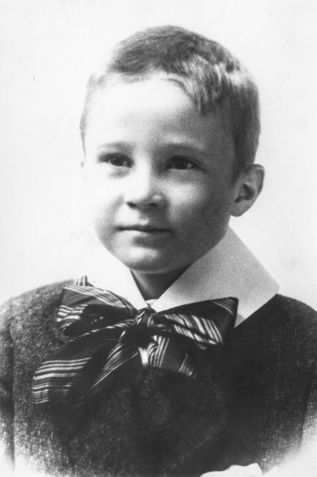 Black and white archival photograph of a boy wearing a sweater, a white collar, and a bow tie tied under his chin.