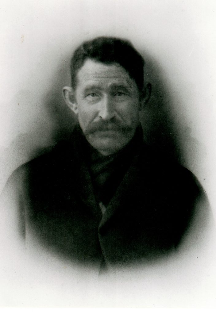 Photographie d’archive en noir et blanc d’un homme moustachu en costume-cravate.