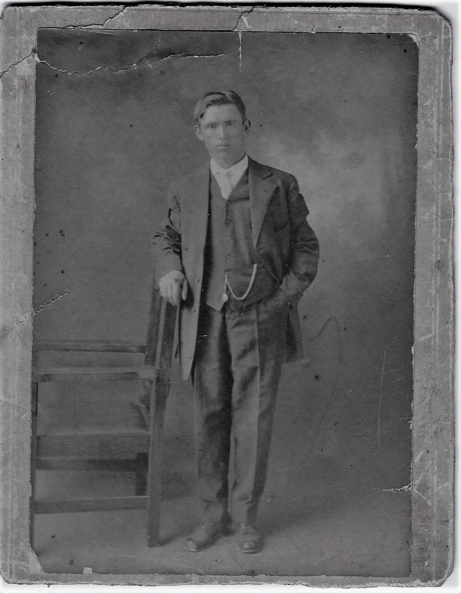 Black and white archival photograph of a man wearing a suit and tie and leaning on a chair.