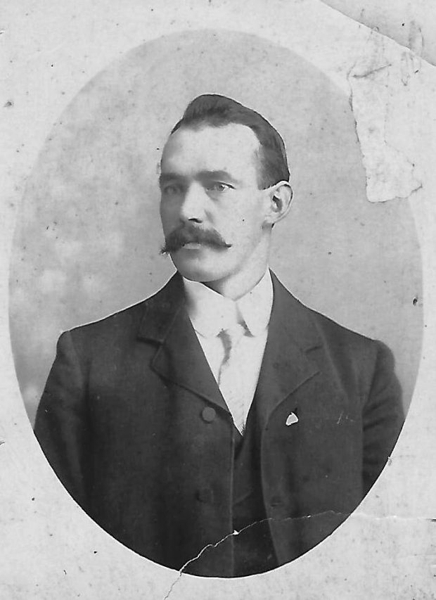 Black and white archival photograph of a man with a moustache wearing a suit and tie.