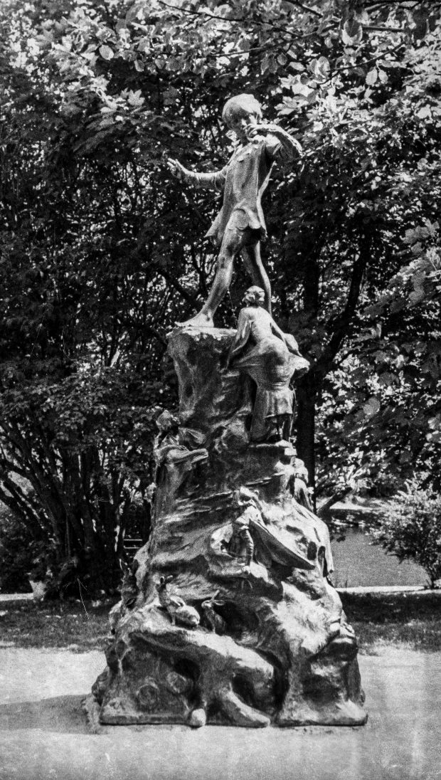 Black and white photograph of Peter Pan Statue. Tall statue with animals, people, and a boy standing on top.