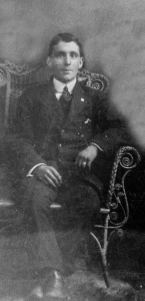 Black and white archival photograph of man sitting in a chair wearing a suit and tie.