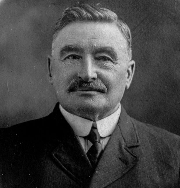 Black and white archival photograph of a man with a moustache wearing a suit and tie.