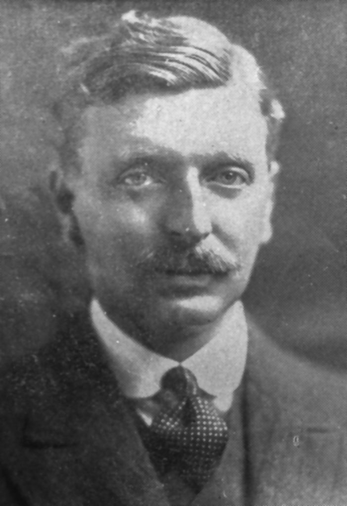Black and white archival photograph of a man with a moustache wearing a suit, and tie.