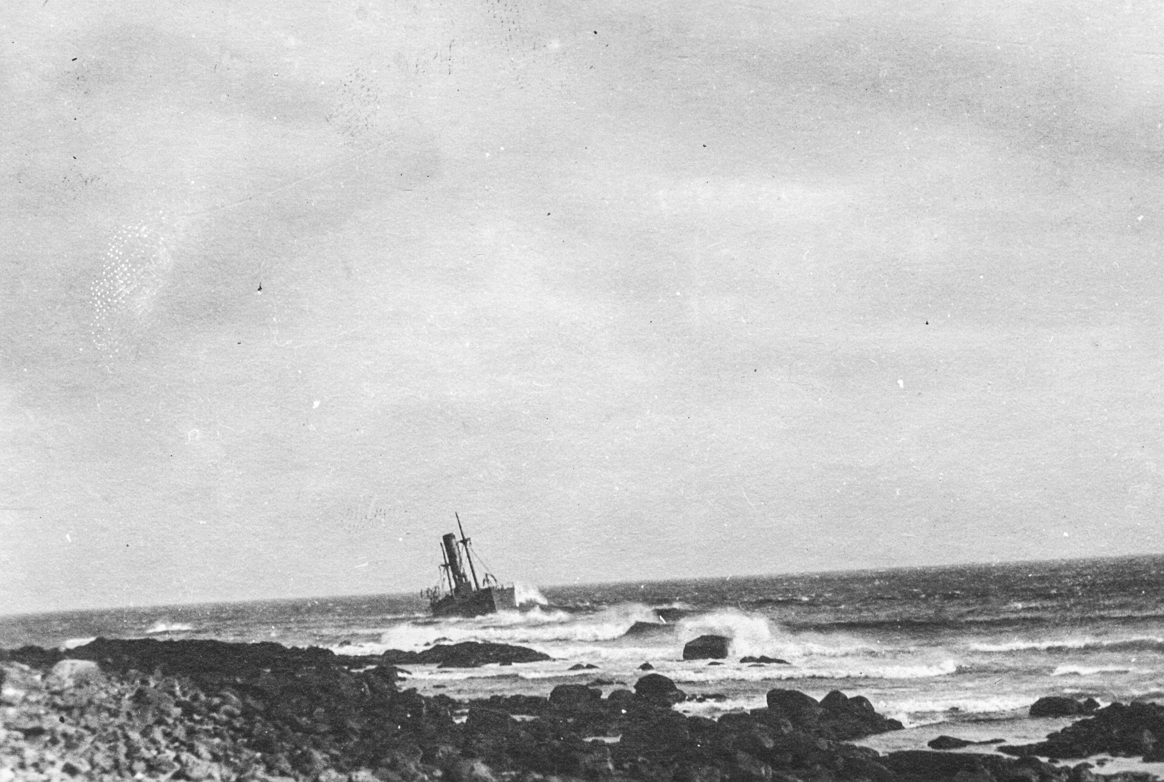 Black and white archival photograph of large passenger liner ship, the SS Florizel, run aground just offshore from rocky beach.