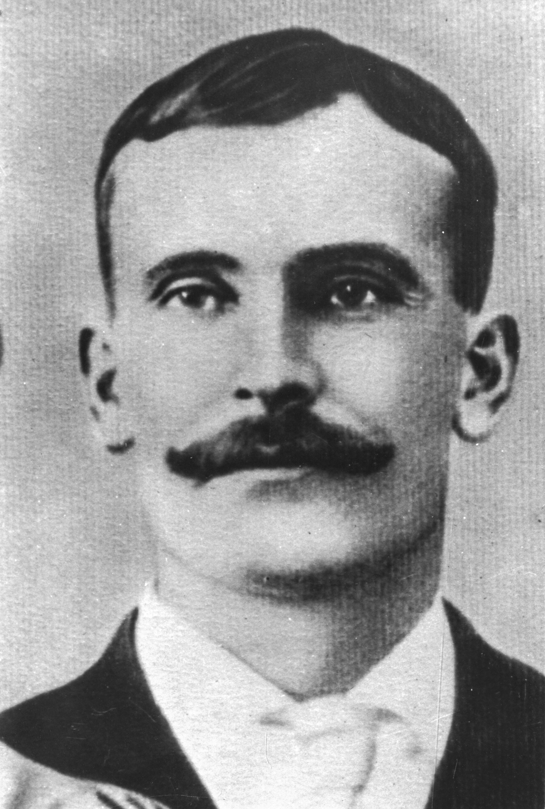 Black and white archival photograph of a man with a moustache wearing a suit, and tie.