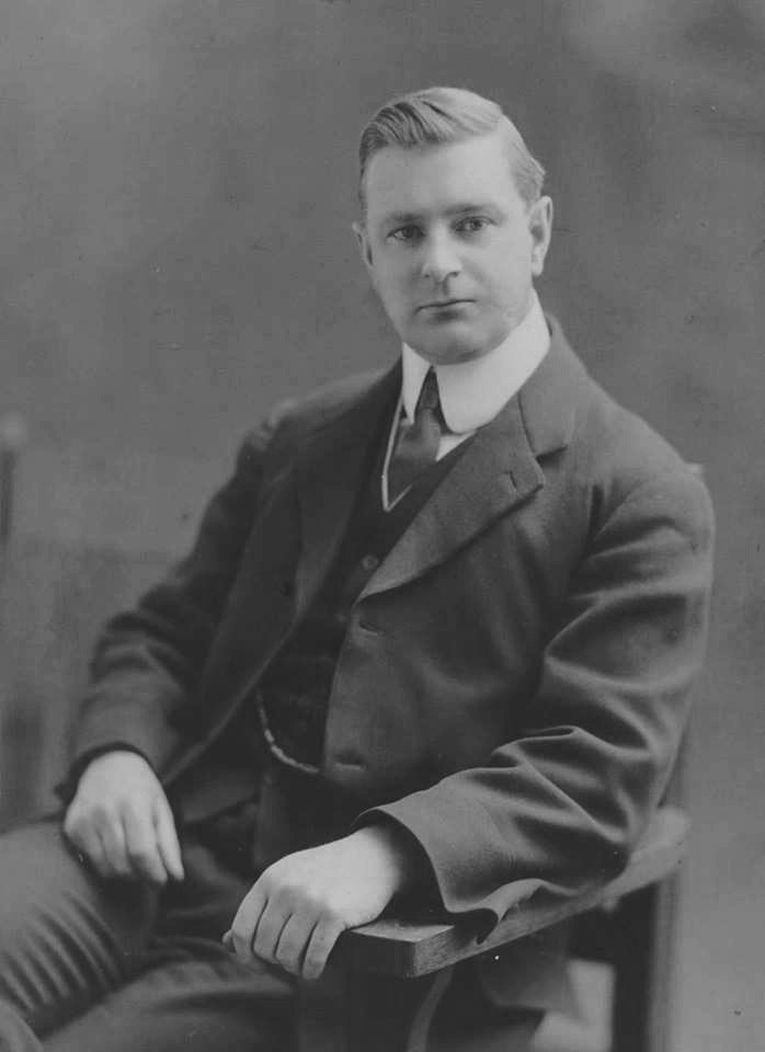 Black and white archival photograph of man seated in chair wearing a suit, and tie.