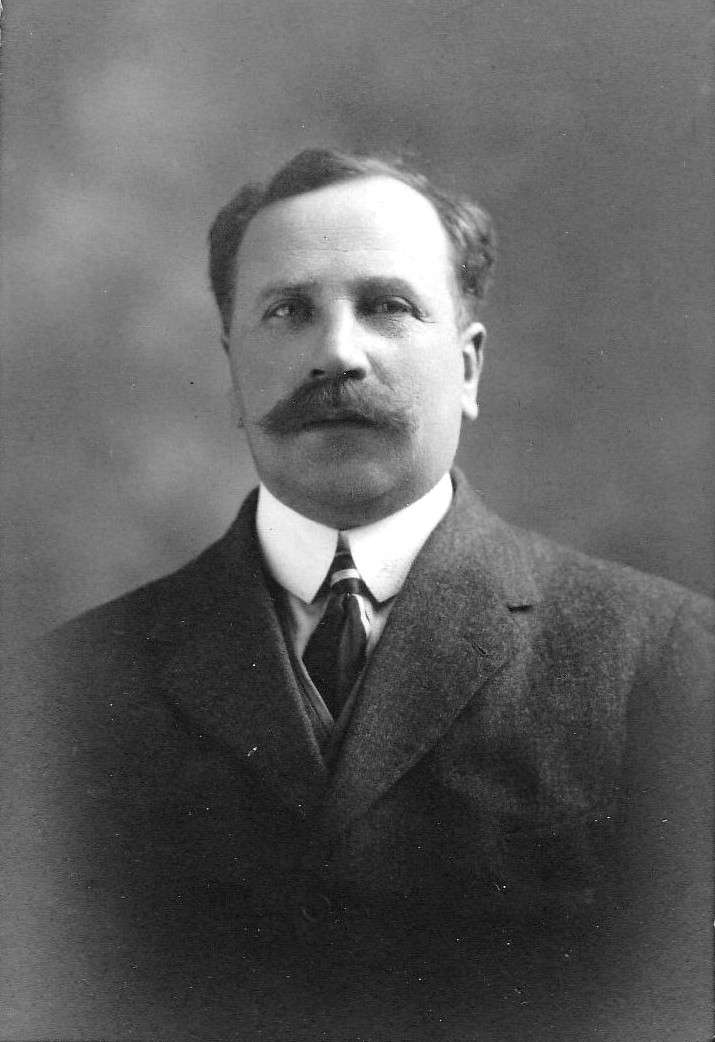 Black and white archival photograph of a man with a moustache wearing a suit, and tie.