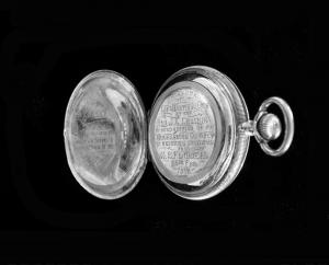 Black and white modern photograph of open gold watch with inscription on one side.