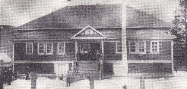 It is winter and children are gathered on the wide steps of a school. Several children are playing in the snow in the schoolyard.