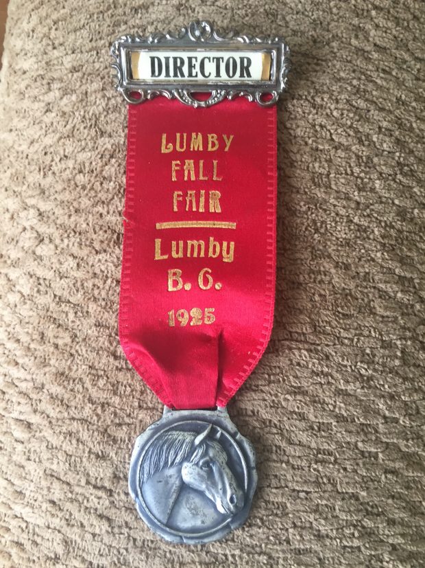 A Director’s badge has a red ribbon that says “Lumby Fall Fair Lumby BC 1925”. There is a metal with a horse head attached to the ribbon.