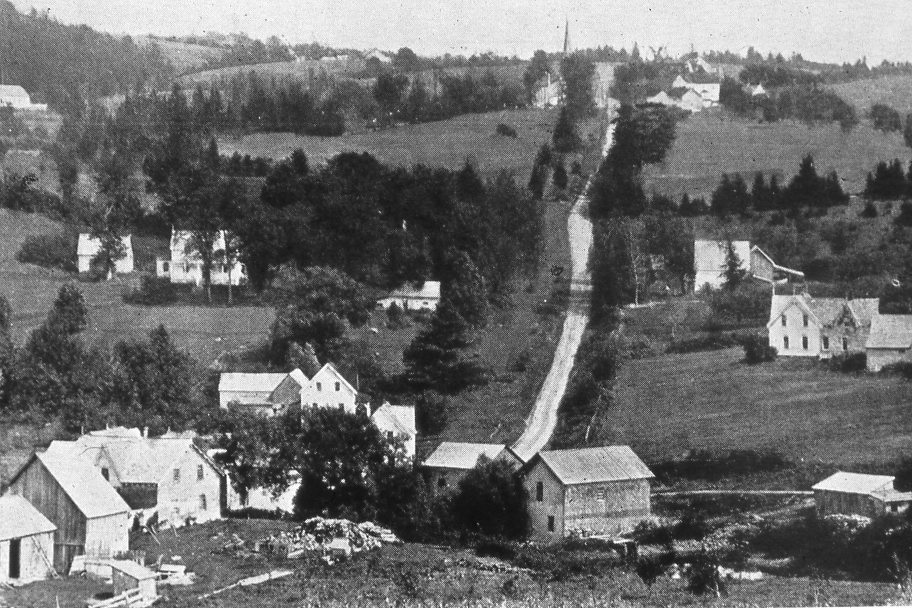 Circa 1900. Rural scene shows a church in the distance at the top of the hill. Homes and farms appear on either side of the steep hill down to the lower part of the town.