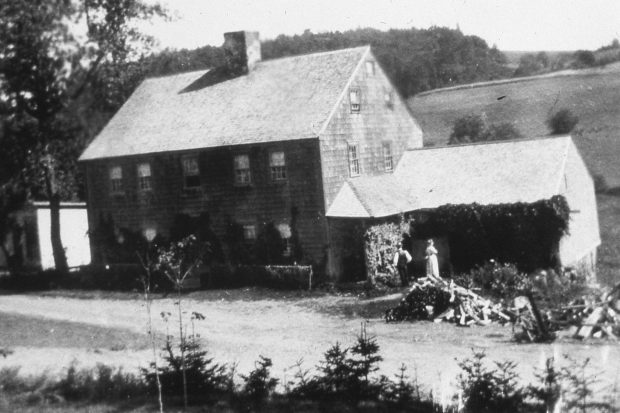 A two story residence with an attached one story wing to the right. A man and a woman stand in front of the wing.