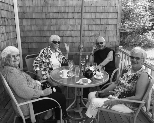 Three senior females and one senior male sitting at a restaurant patio table under an umbrella.